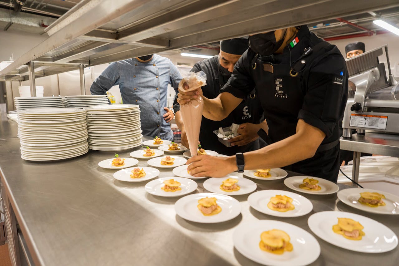 Chefs work meticulously plating gourmet dishes in a bustling professional kitchen.