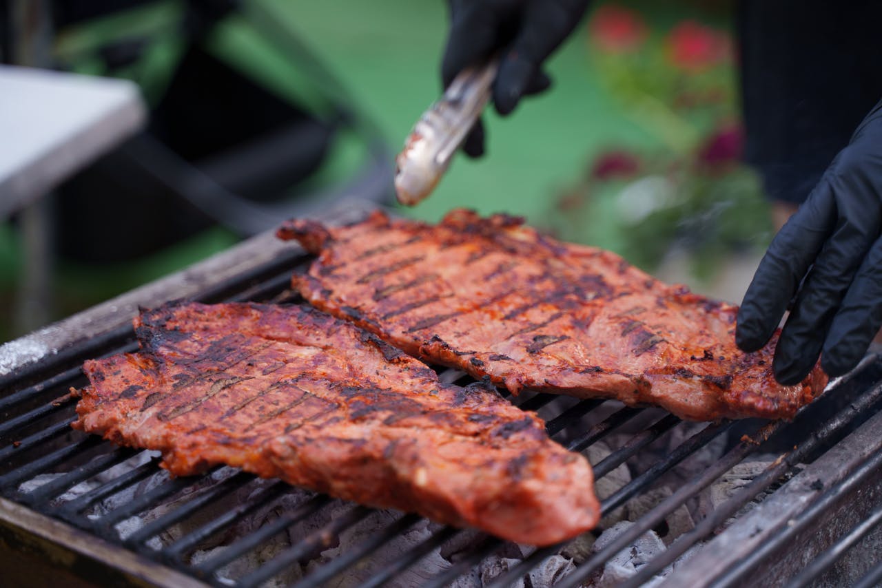 Offerings Close-up of juicy grilled meat cooking on an outdoor BBQ with tongs handling ribs.