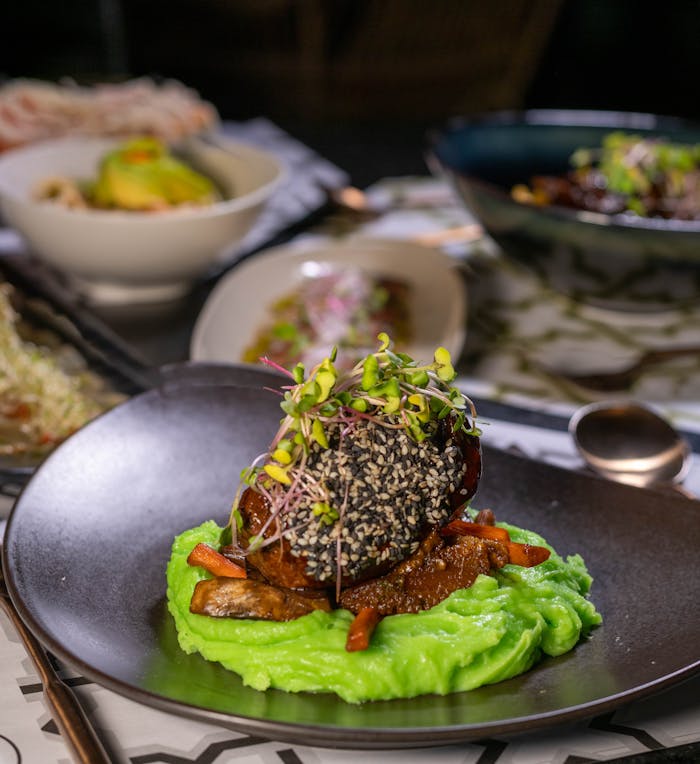 Exquisite gourmet meal featuring sesame-topped meat and vibrant green puree, artfully plated.
