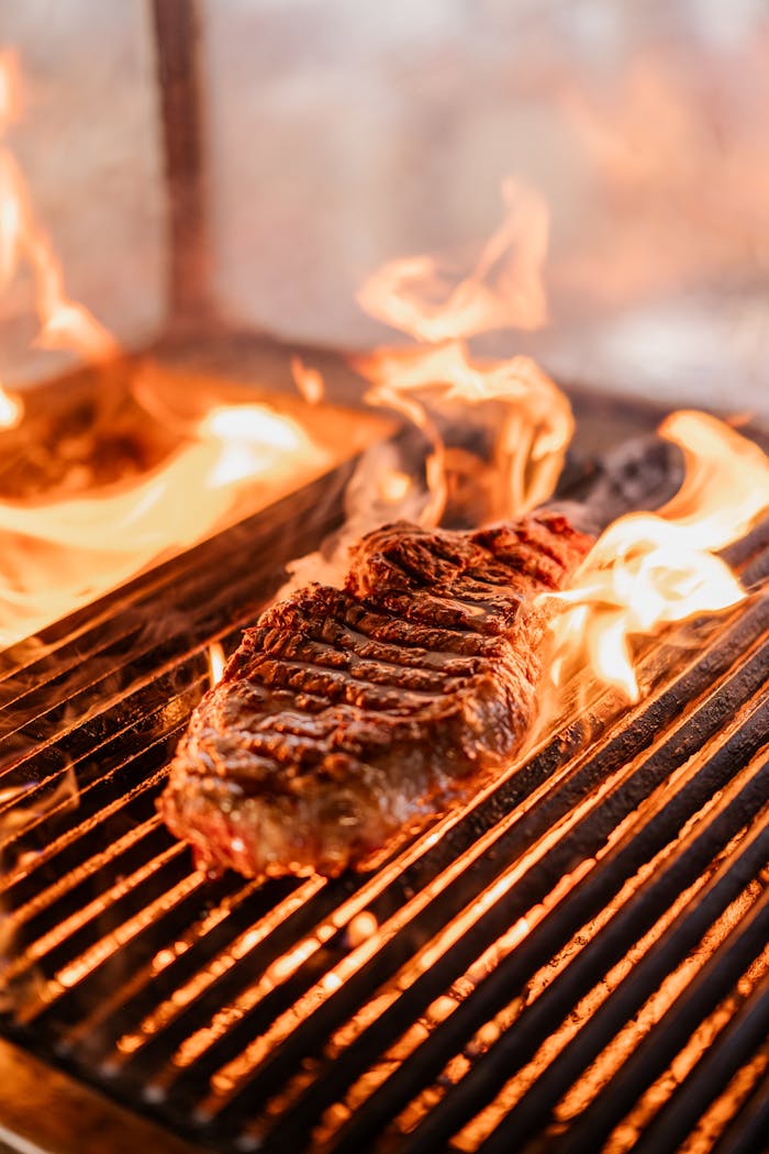 Offerings Close-up of a juicy steak sizzling on a hot grill surrounded by dancing flames.