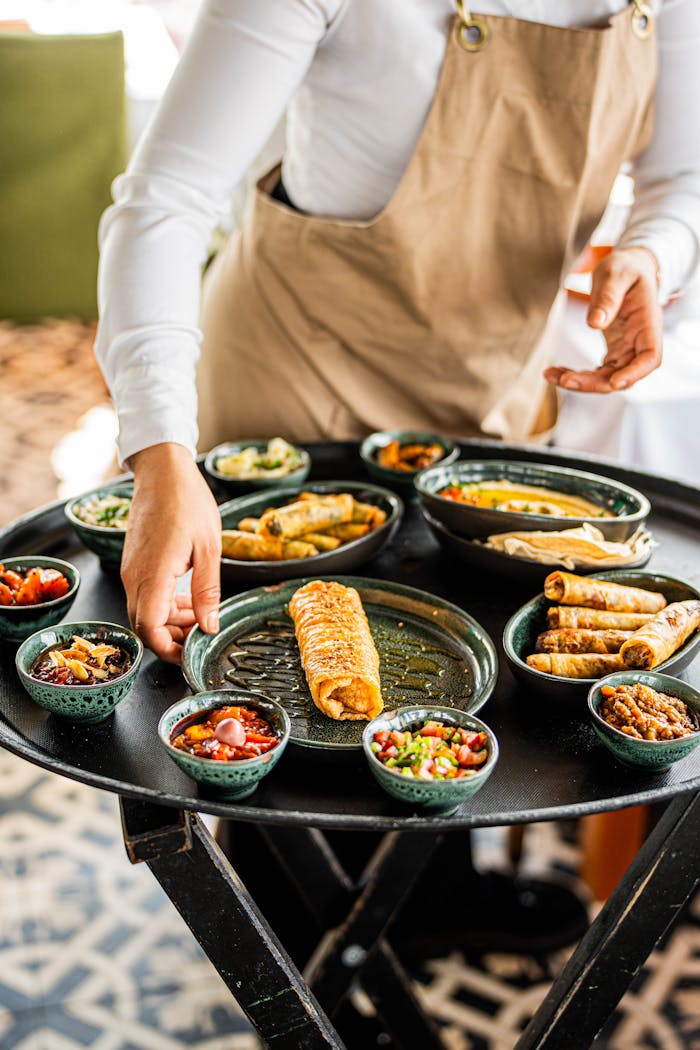 Waiter in apron serves variety of Mediterranean dishes on a large round tray, offering diverse flavors and vibrant colors.