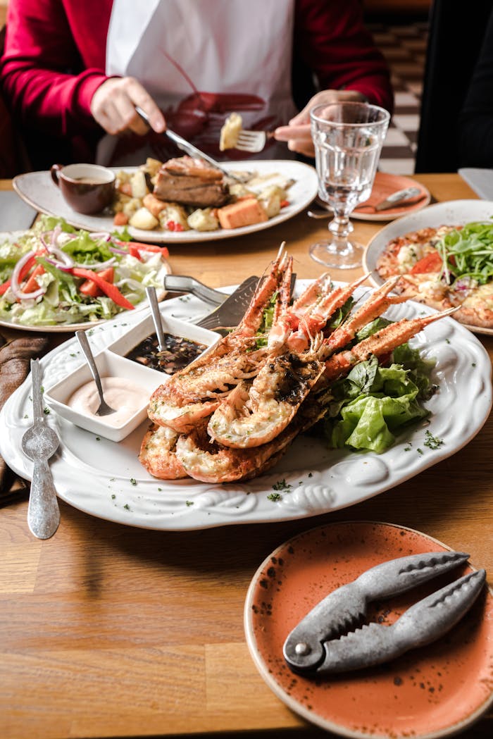 From above unrecognizable customer enjoying gourmet dinner with lobster and meat dish sitting at wooden table with assorted traditional dishes