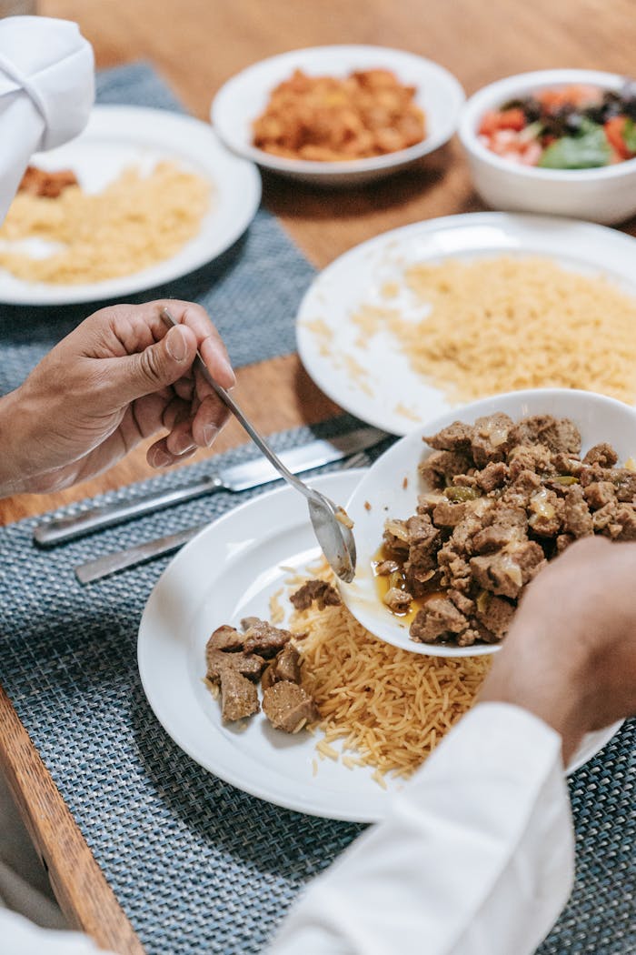 A close-up of a delicious meal with meat and rice being served by hands on a dining table.